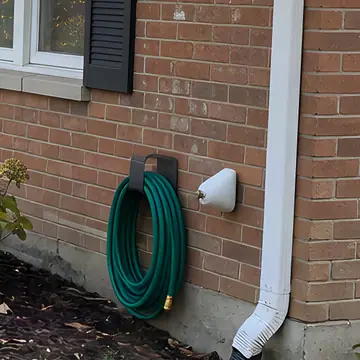 A coiled hose on a wall hanger next to a foam-covered outdoor faucet